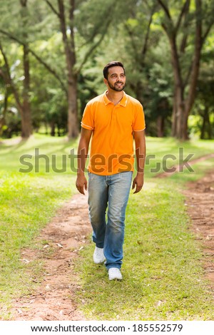 casual young indian man walking in the park and looking away