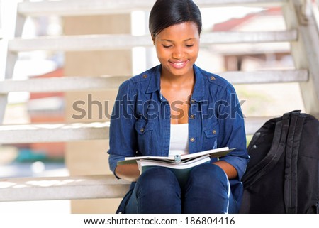 smart african american university student reading a book outdoors