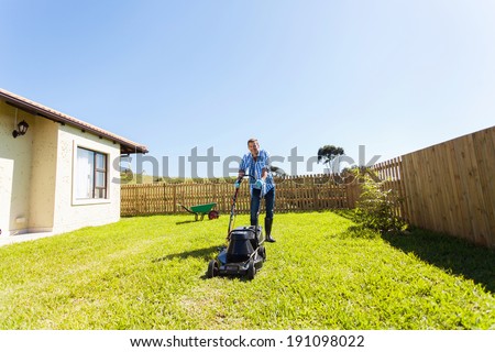 cheerful young man mowing lawn at home