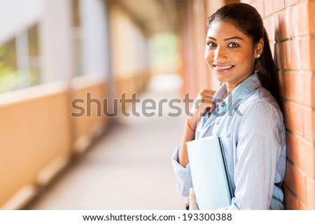 happy indian college student leaning against wall