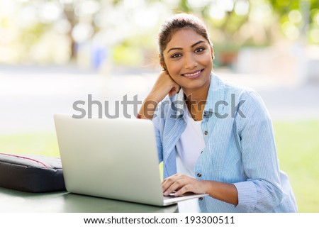 pretty indian university student using laptop computer outdoors