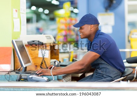 happy african male cashier working at till point in supermarket