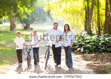 happy indian family of four walking outdoors in the park