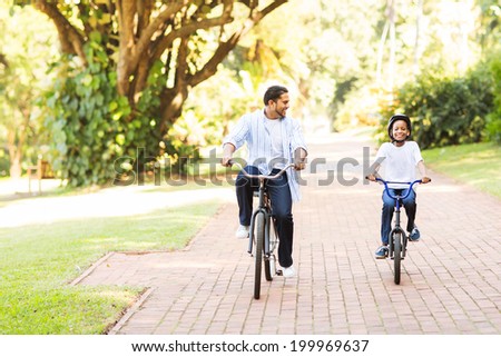 cheerful indian father and daughter riding bikes in the park