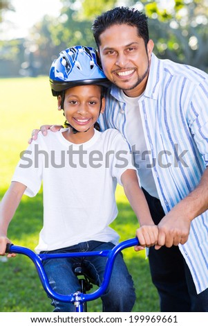 young indian girl on a bike with her father standing next to her