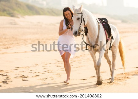 cheerful young woman walking with a horse on beach in early morning