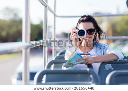 young female traveller taking photo of the city from an open top bus