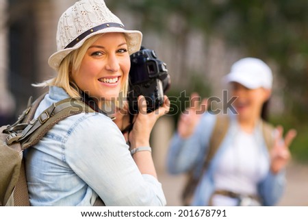 happy young tourist taking a photo of her friend with digital camera