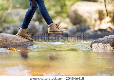 young woman hiking in mountain crossing stream