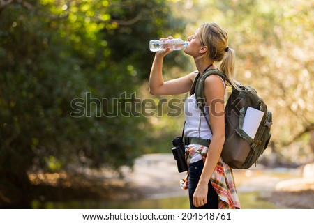young hiker drinking water at mountain valley