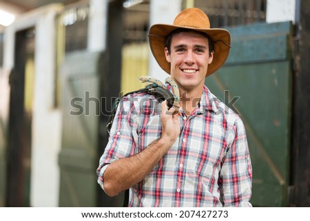 happy cowboy carrying reins of a horse inside stables