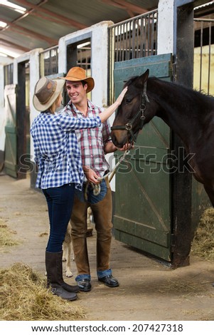 happy cowboy and cowgirl couple inside stables with their horse