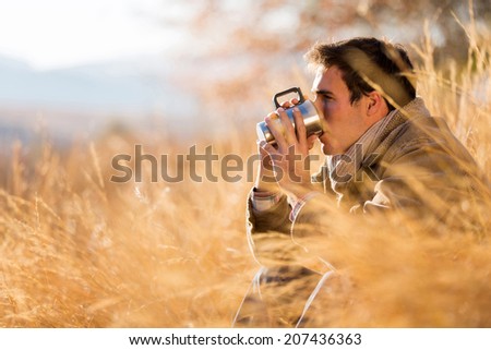 peaceful young man drinking coffee in autumn by the lake