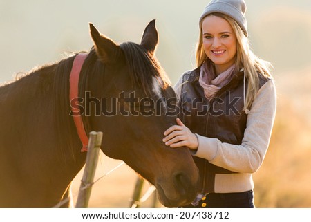 cheerful young woman petting horse in the ranch