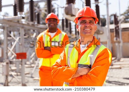 handsome middle aged electrical worker looking up with colleague on background
