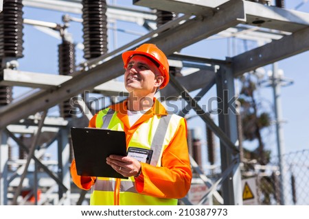 happy middle aged electrical engineer with clipboard in substation