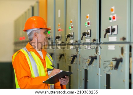 senior technician writing results of measurements in power plant control room