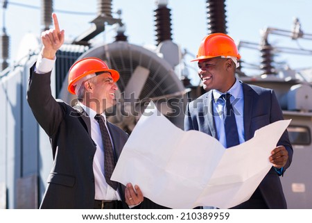 happy managers discussing blueprint at electrical substation