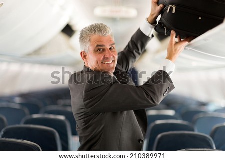portrait of middle aged business traveler putting luggage into overhead locker on airplane