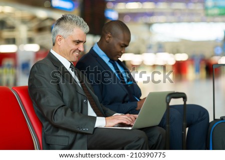 smiling middle aged businessman using laptop computer at airport