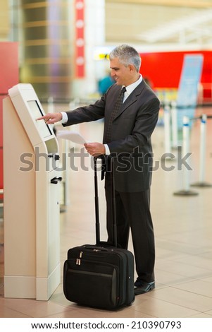 middle aged businessman using self help check in machine at airport