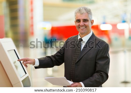happy mature businessman using self help check in machine at airport