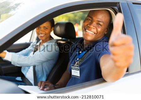 happy male african driving instructor in a car with learner driver giving thumb up
