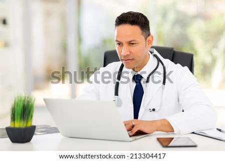 professional mid age medical doctor using laptop in office
