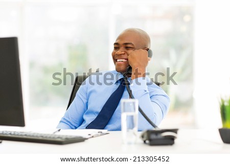 cheerful afro american businessman talking on landline phone in office