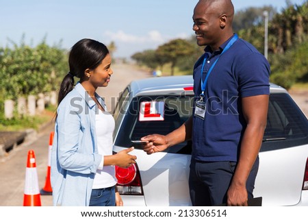 friendly african driving instructor handing driving license to student driver