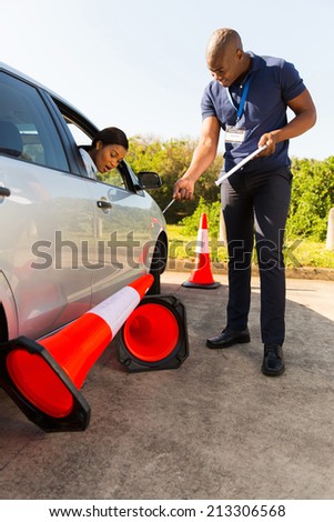 african woman taking driving lessons and running over traffic cone