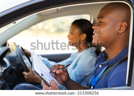 african american driving instructor inside a car with student driver