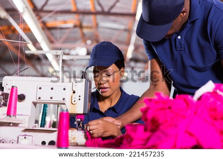 textile factory foreman helping young sewing machinist in clothing factory