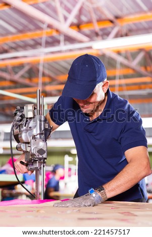 skilled middle aged factory worker using fabric cutter