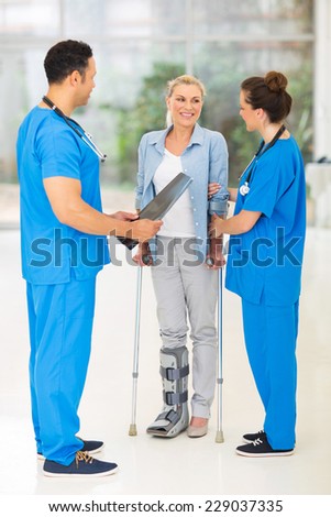 friendly healthcare workers with injured woman on crutches in hospital
