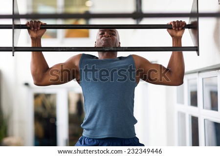 strong african man doing pull-ups on a bar in a gym