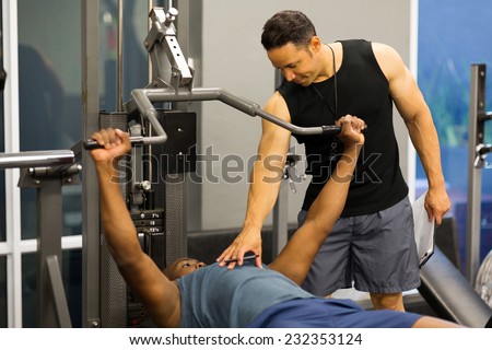 personal trainer helping client lift weights at the gym