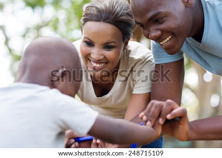 caring african couple helping their little son to ride bicycle outdoors