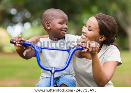 pretty young african woman helping her adorable son ride a bike