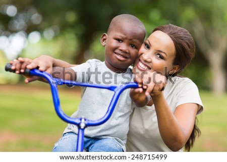 caring african american woman helping her son to ride a bike in park