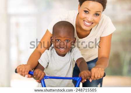 cheerful african mother teaching son to ride a bike