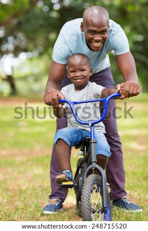 loving african father helping son ride a bike outdoors