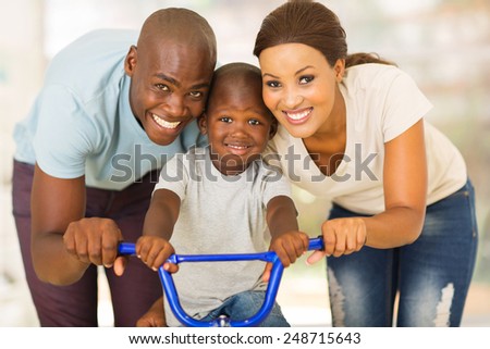 lovely african couple teaching son to ride a bike at home