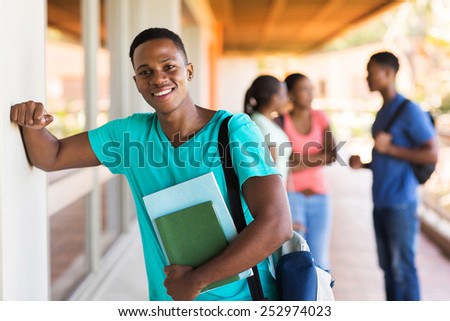 cheerful african college boy with books standing by passage
