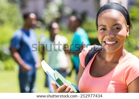 pretty female african college student holding books on campus