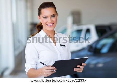 young car saleswoman holding clipboard in showroom