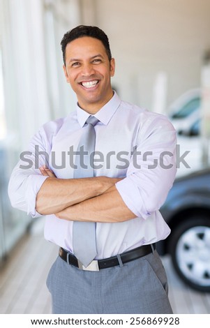 good looking vehicle salesman with arms crossed in car showroom
