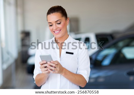 beautiful young car sales consultant using smart phone at showroom