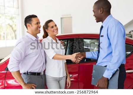 beautiful couple handshake with car salesman after purchasing a car