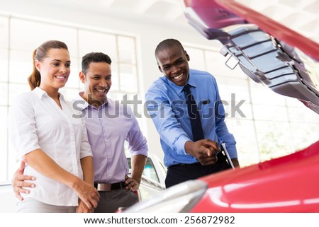 happy african car salesman showing car engine to customers